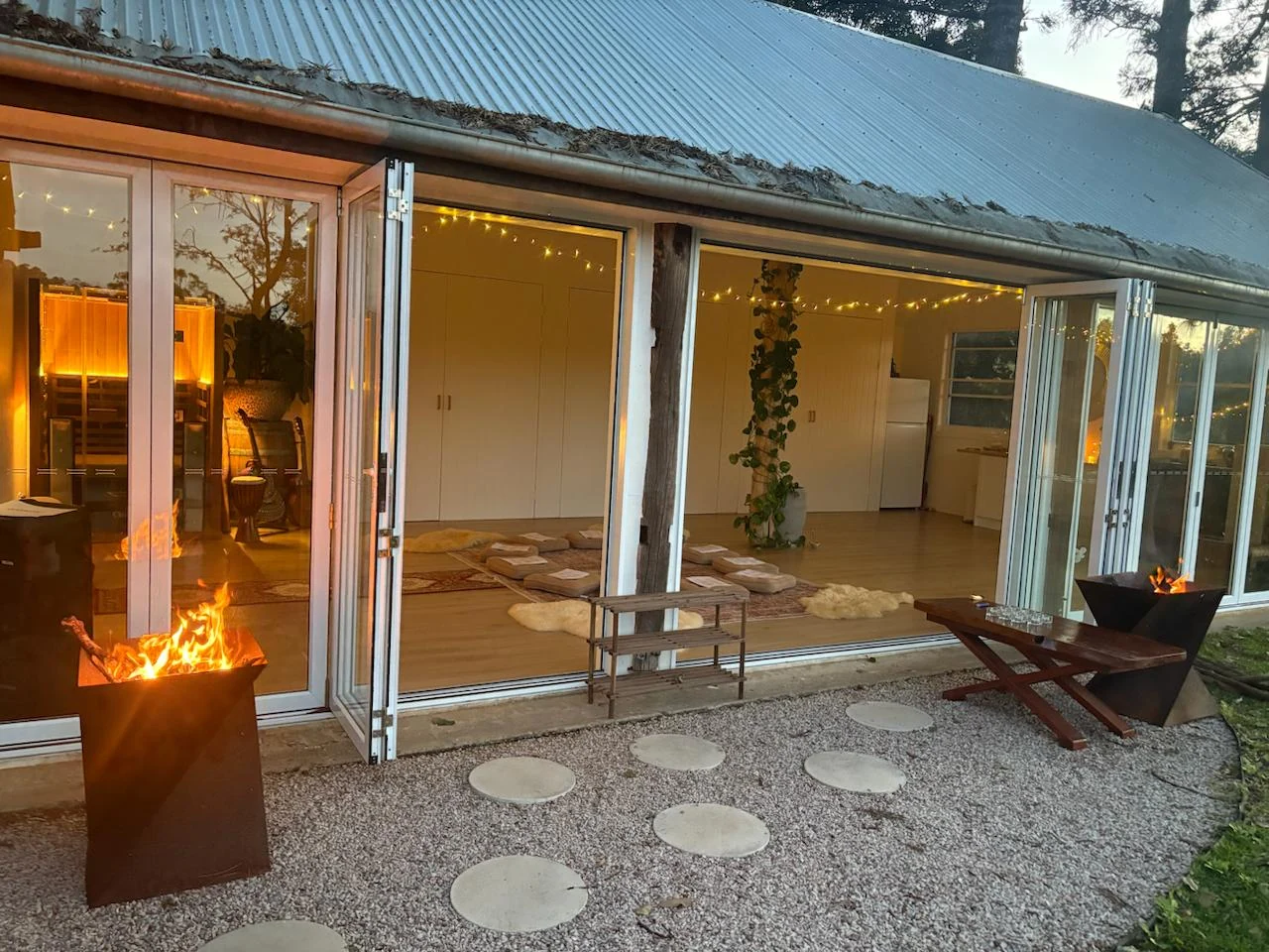 The shala at dusk, doors open wide, fire bowls burning.